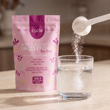 Powder pouring from the exact-dose scoop into a glass of water, Cycla pouch behind